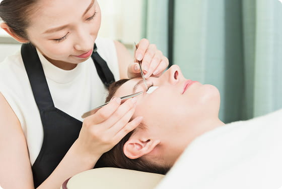 施術者がリクライニングチェアに横たわる女性にまつげエクステを施している