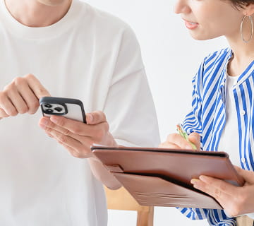 スマートフォンを見せる人物と、タブレットにメモを取る人物のやり取り