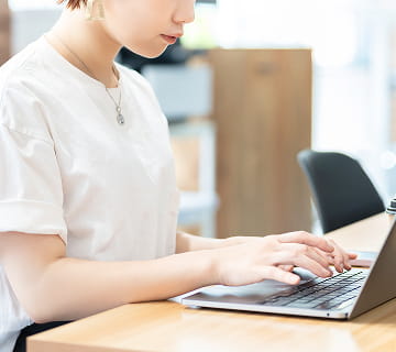 白いTシャツを着た女性がノートパソコンでタイピングしている