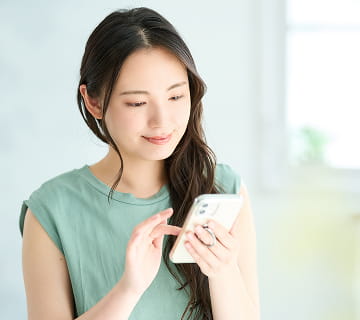 ミントグリーンの服を着た女性がスマートフォンを操作している